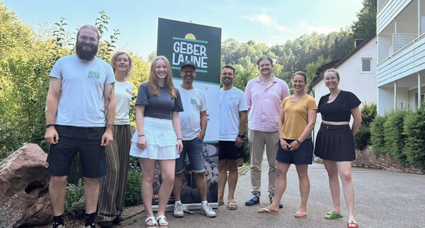 Gruppe von acht Personen vor einem Werbeschild "Geber Laune" im Freien.